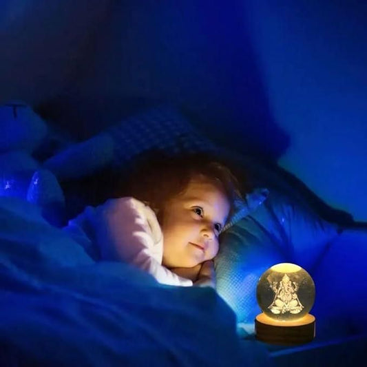 Ganesh Crystal LED Lamp - Shoppingstore25Shoppingstore258121759318A young child lies in bed at night, illuminated by the soft blue glow of a Ganesh Crystal LED Lamp and a glowing snow globe with a figurine inside, gazing at it with a dreamy expression.