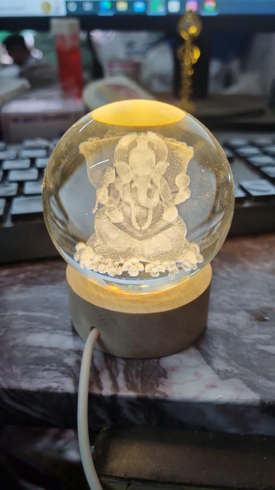 Ganesh Crystal LED Lamp - Shoppingstore25Shoppingstore258121759318The Ganesh Crystal LED Lamp features an etched image of Lord Ganesha on a lit wooden base, placed in front of a computer keyboard and monitor with a white cable attached.